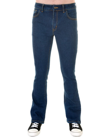 Model is stood in front of a white studio background wearing the stonewash stretch denim slim bootcut jeans with black trainers. They are facing forward and photo is cropped from the waist down.