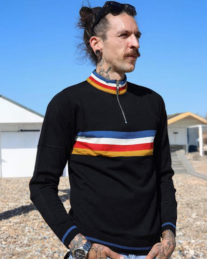 Tattooed model is standing in front of a bright blue sky with sunglasses on his head and wearing the Black Lightning Rainbow Cropped Jumper.