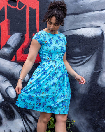 Georgia is stood in front of a graffiti wall wearing the cherry blossom black belted stretch tea dress with pockets with flame socks and black converse. She is facing forward posing