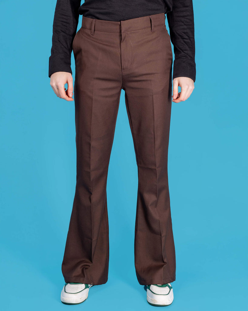 Jack is stood in front of a blue studio background wearing the Presley brown bell bottom trouser slacks with a long sleeve black tshirt and white trainers. They are facing forward posing with both arms resting by their sides. Photo is cropped from the waist down.