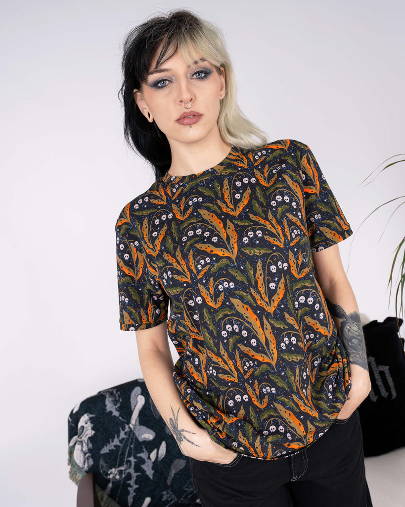 A model styled in the Run & Fly Halloween Poison and Plants T-shirt, casually posing with hands in pockets. Featuring Clare Lewis’s design of orange leaves, skulls, and starry details, this ethical fashion piece is perfect for spooky season and beyond.