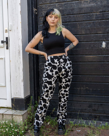 Front-facing image of the model wearing black and white cow print jeans from Run & Fly. The straight-leg fit and high-waisted style are paired with a black crop top, making the quirky cow print stand out. Ethically made by a small, slow fashion brand, these jeans offer a fun, eco-friendly style option.