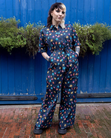 Claudia a model with a half black half blonde mullet is wearing a jumpsuit with fairy lights on stood against a blue door in a mews in hove. 