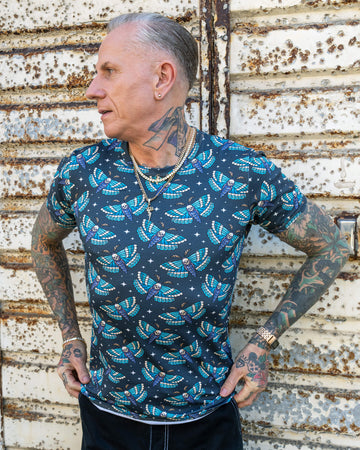 James, wearing the “Death Head Moth” t-shirt by Run & Fly, turns slightly, displaying the full moth pattern across his back and sleeves. The blue and white moths with skull details create a bold, alternative look.