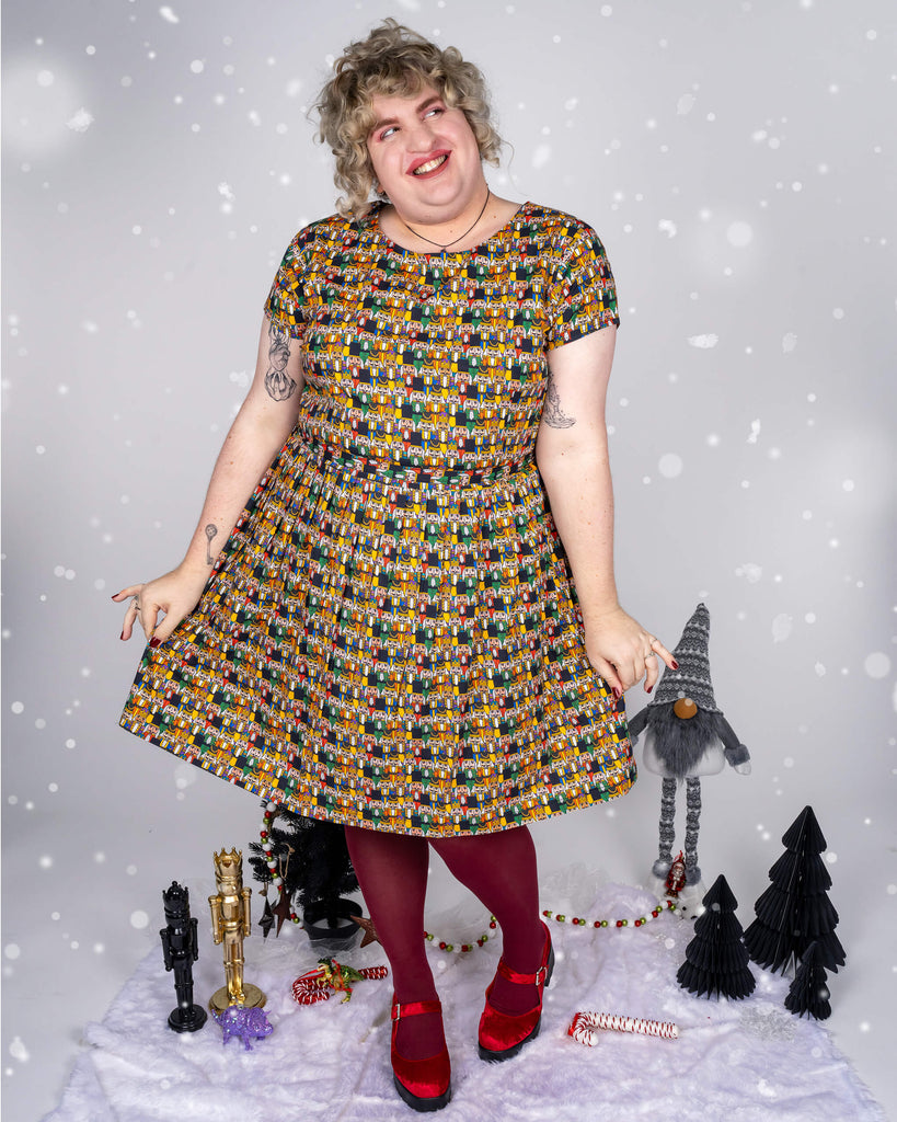 Close-up of Maddie’s expression, showing excitement with hands near the collar of the Nutcracker print dress. Maddie’s curly hair, bold makeup, and joyful look add a fun holiday vibe to the image, against a light, snowy background.