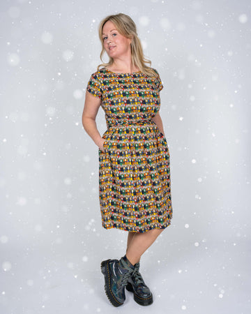 A playful pose of the model wearing the Nutcracker dress, hands in pockets, and looking sideways. The festive design and snowy white background add to the holiday vibe.