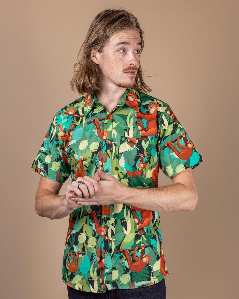 Model wearing a Run & Fly Orangutan Short Sleeve Shirt, showcasing a vibrant tropical print with playful orangutans on a green jungle background. The model poses in a relaxed stance, highlighting the ethical slow fashion brand’s commitment to bold, unique designs. Perfect for animal lovers, this shirt combines sustainable style with a quirky, nature-inspired aesthetic.