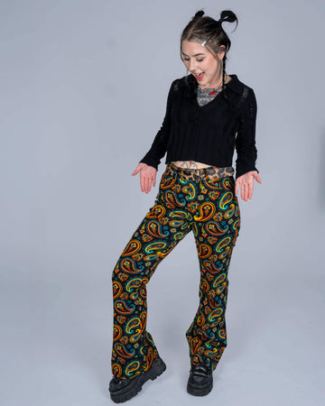 Model animatedly posing in bold paisley print flared trousers and a black knit top, adding a playful touch to the studio setting.