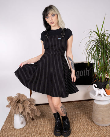 Model twirling in the Run & Fly Black & White Pinstripe Flared Pinafore Dress. The flared skirt showcases movement, and the pinstripe pattern adds a touch of vintage-inspired sophistication to this ethical slow fashion piece.