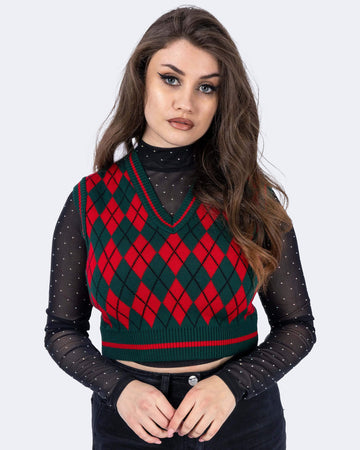 Charlotte is wearing Red and Green Argyle Knitted Tank Top with a long sleeve black mesh top underneath with white polka dots and black trousers. Charlotte is stood in front of a white background posing toward the camera with her hands together. The photo is cropped from the thighs down. 