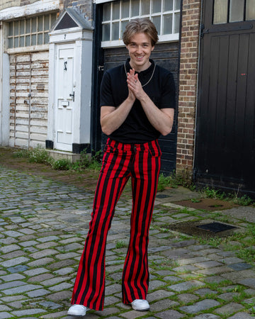 Jack is stood outside in Hove in a mews wearing Red & Black Striped Bell Bottom Stretch Super Flares with a black tshirt tucked in and white trainers. He is facing the camera and smiling with his hands together in front of him.