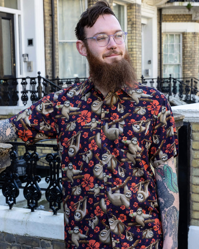 Declan a male in his 20's with a beard and glasses is wearing a sloth shirt with Hawaiian flowers on and beige cargo trousers on a street in Hove.