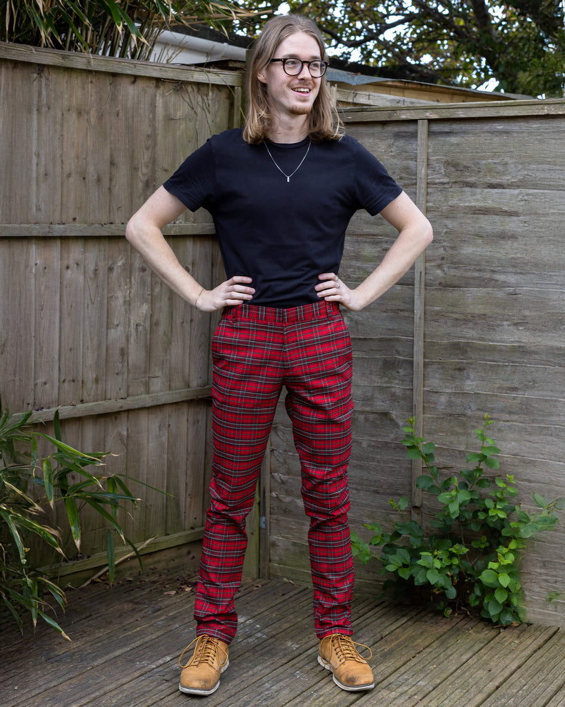 Jack is stood in a garden wearing the retro mod stretch red royal Stewart tartan trousers with a short sleeve black shirt and white trainers.