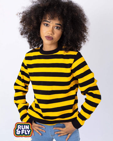 Cindy is stood in front of a white studio background wearing the yellow and black striped jumper with blue denim jeans. They are facing forward posing with both hands resting on their front jean pockets. Photo is cropped from the hips up.