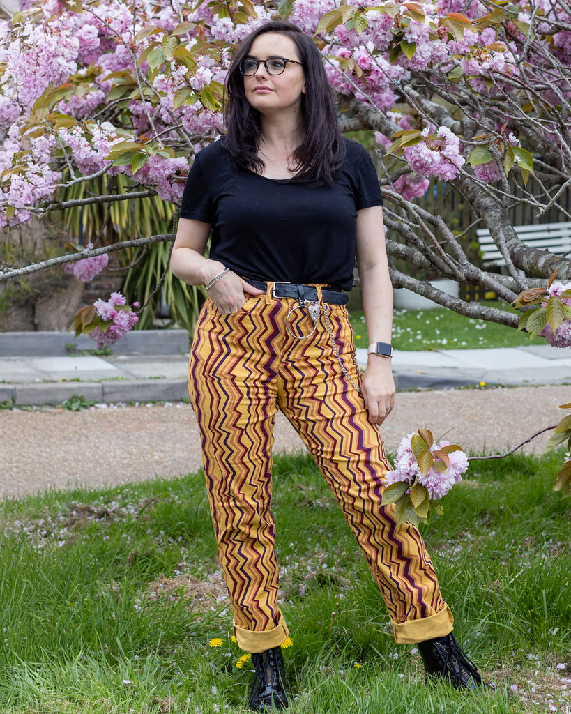 Amy is wearing the 90's zigzag straight leg high waisted jeans with a long sleeve black tshirt and yellow black boots looking smiley in front of a blossom tree